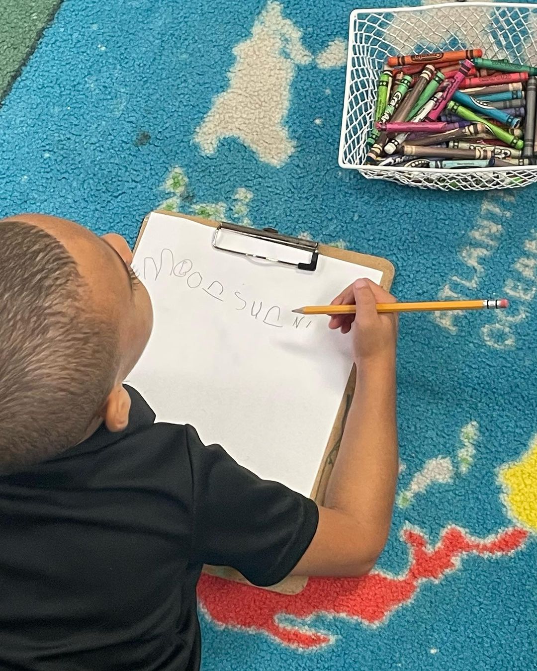 a boy is writing on the floor with a clipboard